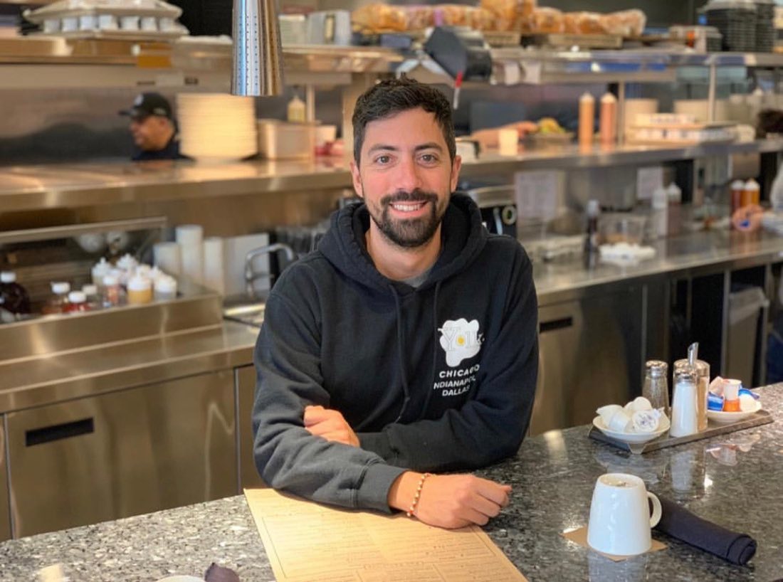 Gianluca Pesce, Yolk Catering Manager, seated at the counter of a Yolk restaurant in front of the open kitchen line.